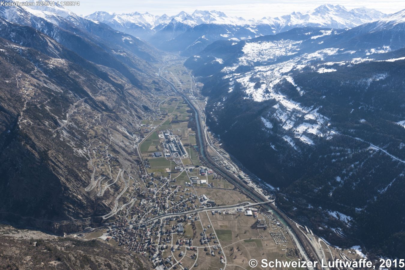 Blickrichtung Rhone - aufwärts; Freizeitflugplatz Raron im Hintergrund. - Dorf im Vordergrund des Bildes: Gampel / Steg. Von hier aus Kehrschleifen zum Lötschberg-Autoverlad. Einfahrt in den Hohtenn-Mittal - Tunnel (Position 2'624'385.09, 1'129'933.91), Richtung Goppenstein. Siedlung SW darunter: Hohtenn. Industrieareal der Lonza-Gampel in der Bildmitte.